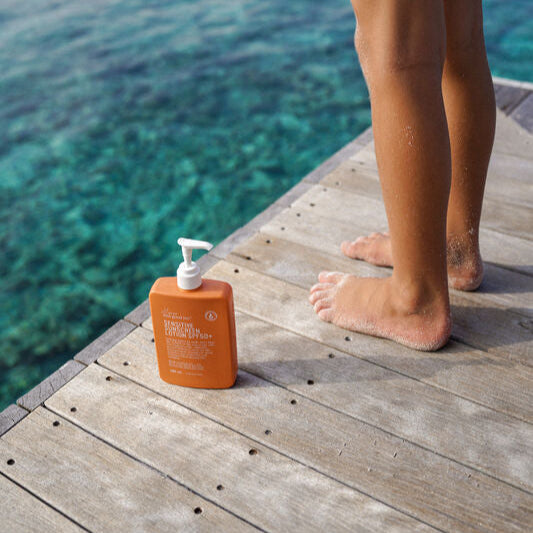 Orange sunscreen bottle on a wooden dock with a child in red shorts standing in the background.