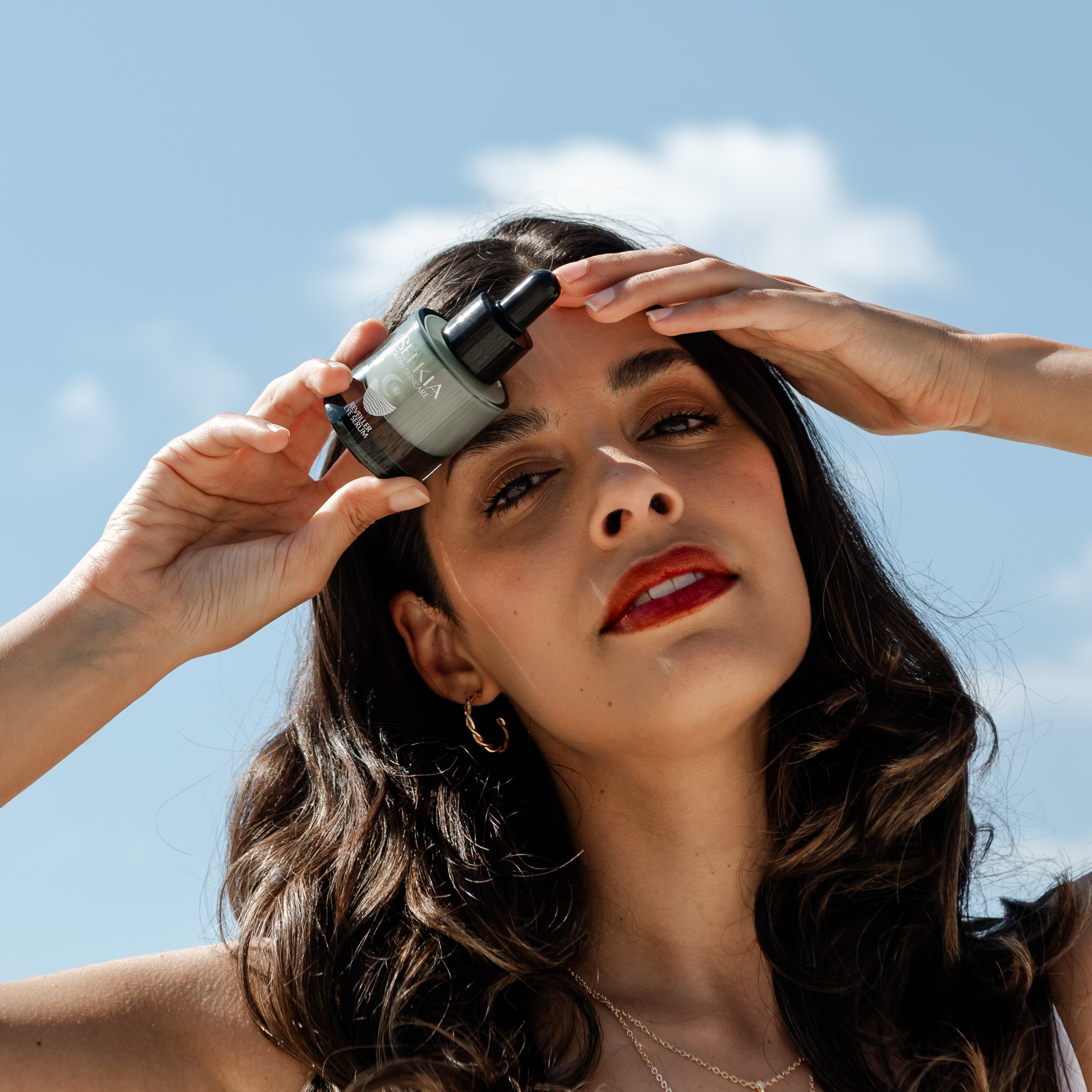 Eye serum bottle in the hand holding on head on woman by the beach