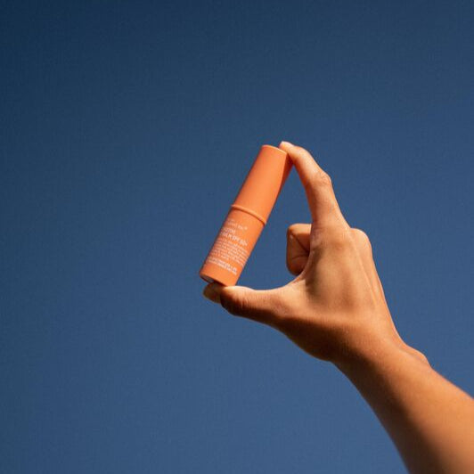 Hand holding two orange cylindrical objects against a blue sky