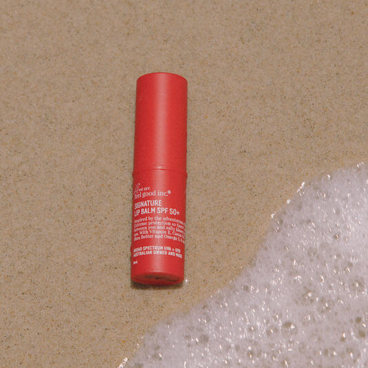 Red lip balm tube on a textured beige surface with bubbles.