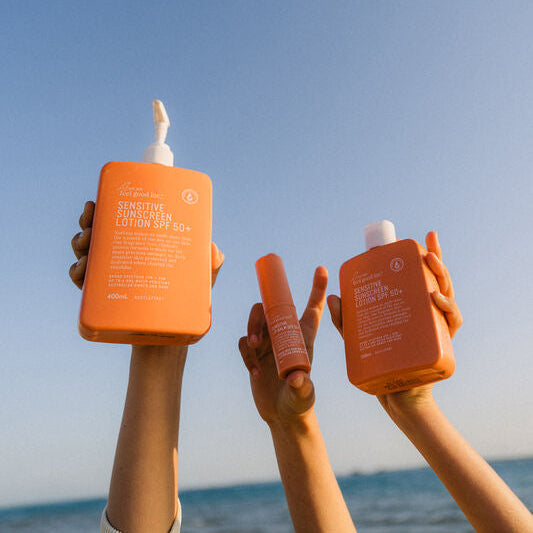 Two hands holding orange bottles against a clear blue sky