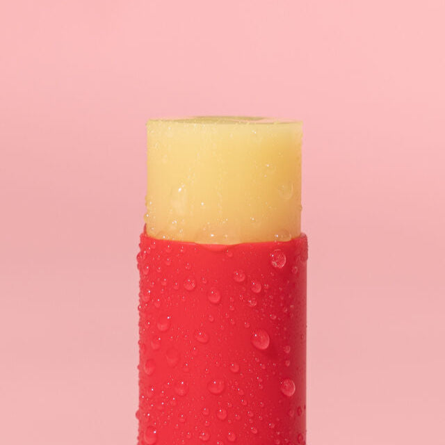 Red and yellow lip balm with water droplets on a pink background