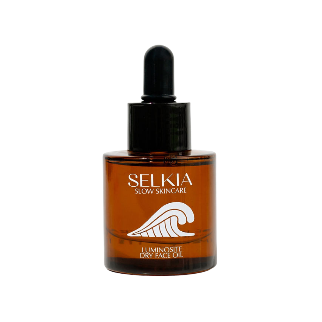 A bottle of SELKIA Slow Skincare Luminosite Dry Face Oil in an amber glass bottle with a black dropper cap, shown on a plain white background.
