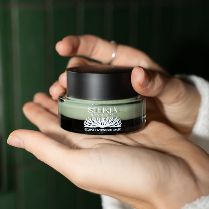 Hand holding a Selkia skincare product with a dark green jar and black lid.